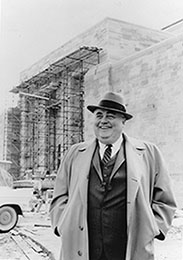 A photo of Herman B Wells standing in front of an unfinished Lilly Library